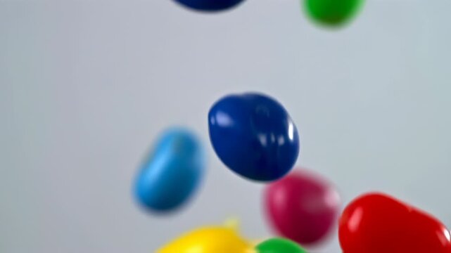 Colorful Glossy Candies Falling and Bouncing Against a White Background in Slow Motion