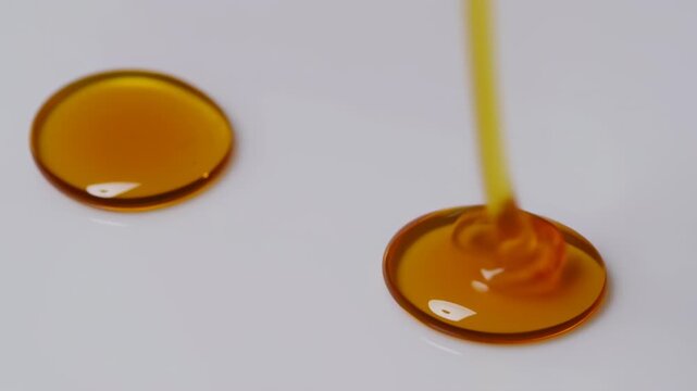 Golden Viscous Liquid Pouring onto White Surface, Forming Drops and Puddles