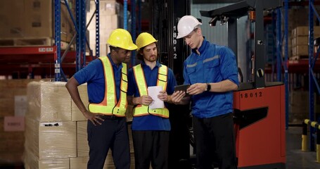 African American male warehouse staff discussing shipment with caucasian supervisor and another logistic worker near forklift and stacked cardboard boxes in modern industrial storage facility - Powered by Adobe