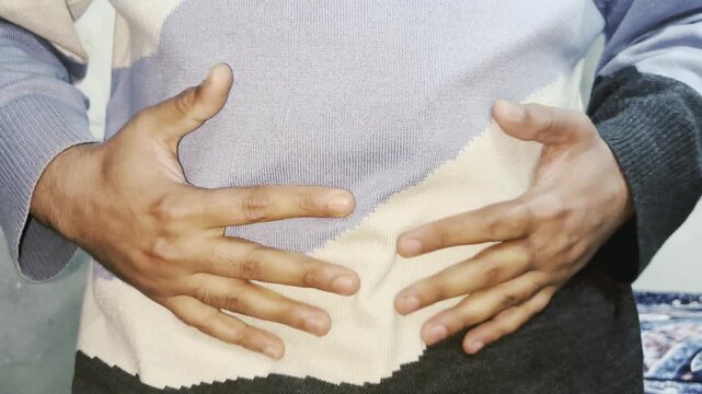 Man having pains in stomach. Young man suffering from a belly ache. Cropped shot of a sick man with an ulcer, IBS, colitis, or dyspepsia holding hands on his abdomen. Health problems concept