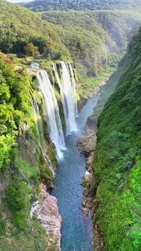 Aerial drone view of Tamul Waterfall cascading down green cliffs into a turquoise pool below. Vertical