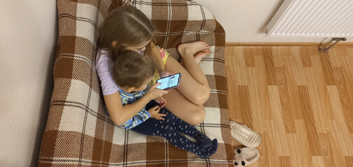 Two young children watching smartphone together on cozy sofa