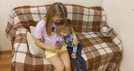 Girl and boy watching video on smartphone while sitting on couch