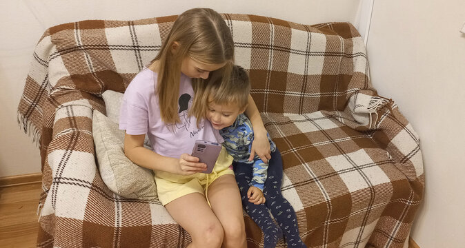 Girl and boy watching video on smartphone while sitting on couch  