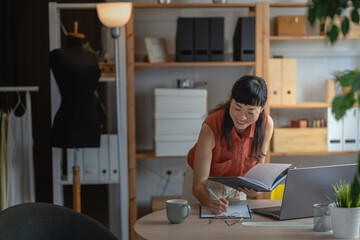 Asian woman small entrepreneur working in her cozy home office, standing at her desk while...