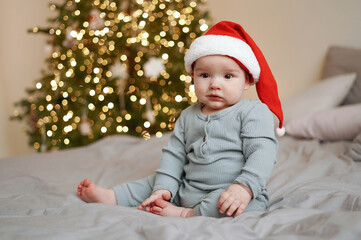 Cute baby in santa hat with christmas tree with blurred lights
