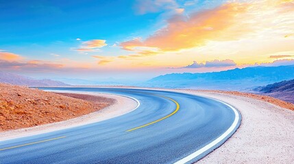A winding asphalt road curves through a desert landscape under a vibrant sunset sky with colorful clouds and distant mountains.