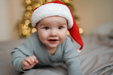 Cute baby in santa hat with christmas tree with blurred lights