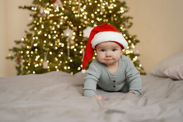 Cute baby in santa hat with christmas tree with blurred lights