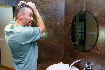 Middle-aged man combing thinning hair in a bathroom mirror. Grooming and aging concept