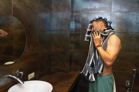 Shirtless muscular man drying his face with a towel in the bathroom. Morning hygiene and self-care