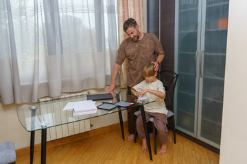 Father watching his son draw at a desk with a graphics tablet. Parent and child creative time at home