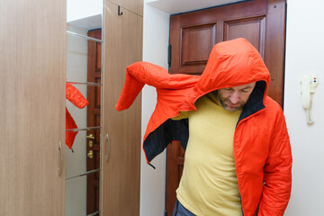 Man putting on a bright orange hooded jacket in a hallway. Getting ready to leave the house