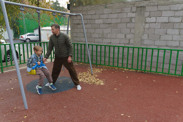 Father pushing his son on a swing at the playground. Family fun in autumn
