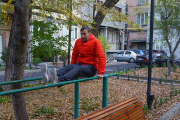Man doing an L-sit exercise on parallel bars in an autumn park. Outdoor calisthenics workout