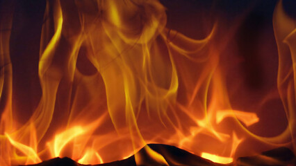 Close up view of warm orange fireplace flames flickering over dark logs, creating a cozy glowing background for winter relaxation, holidays and home comfort.