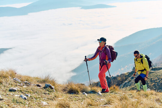 Hikers trek through a stunning mountain landscape above the clouds during a sunny day in early morning