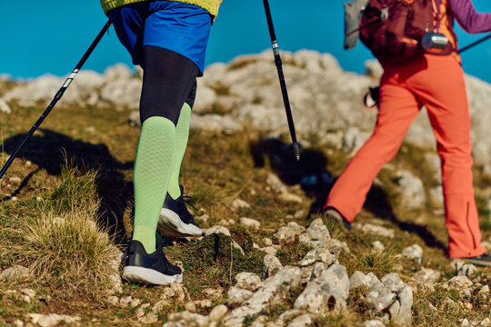 Hiking on rocky trails in the mountains during a clear sunny day with trekking poles and bright active wear
