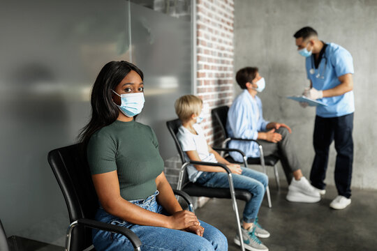 International group of male and female patients waiting for vaccination against COVID-19, having conversation with male doctor african american woman in face mask sitting at hospital hall