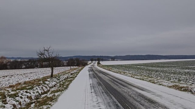 Person walking along a mountain road in a highland region, with compacted and partially melted snow underfoot, capturing the thawing winter atmosphere in rugged terrain.
