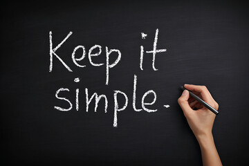 Hand writing the phrase 'Keep it simple' on a black chalkboard with a marker during a creative workshop