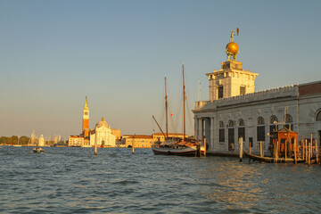 A picturesque view of Venice at sunset: the historic architecture of the waterfront, boats moored along the canal, and the warm golden light reflecting off the water.