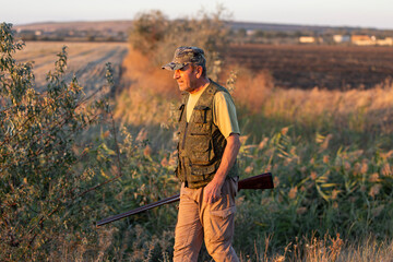 A hunter with a gun in camouflage clothing. A senior man with a gun, medium shot, searching for game.