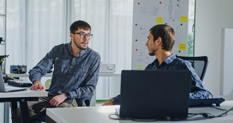 Adult male engineer team discusses AI software development robotic hand project use AI code solutions at tech workspace. Artificial intelligence interface, collaboration support prototype development.