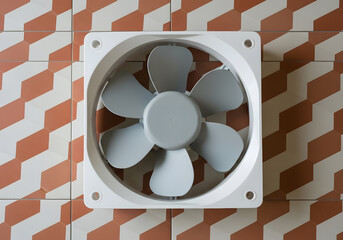 Square white exhaust fan mounted on a patterned terracotta tile wall