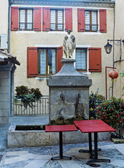 Stone fountain in a small plaza in Sisteron, France, with a rectangular base, two water spouts, and a statue of a robed figure on top.