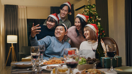 Group of Asia colleague gathering New year holidays party together. Happy friend group mobile phone video call online christmas thanksgiving dinner at home in evening, celebration and people concept.
