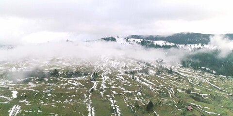 Morning mist above green field with pieces of snow