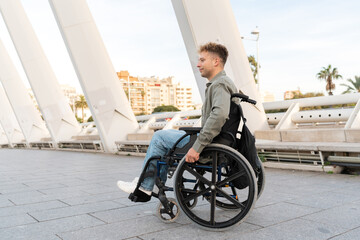 Young adult man using wheelchair moving on urban bridge