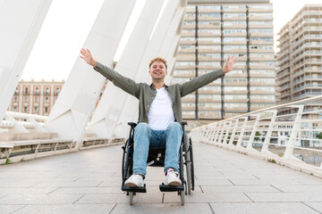 Young man in wheelchair with raised arms enjoying freedom on city bridge