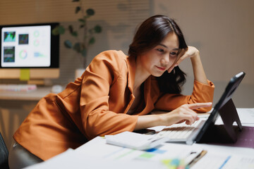 Asian businesswoman working late analyzing data on tablet