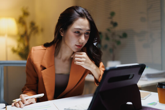 Asian businesswoman working late analyzing data on tablet