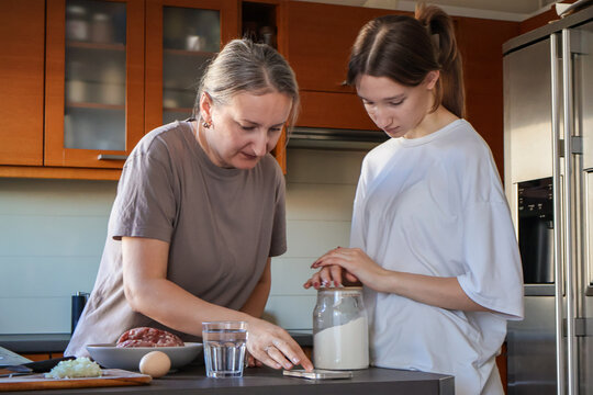 Mother and daughter searching for a recipe on a smartphone. A warm and authentic family cooking together at home, showing two generations preparing traditional dumplings - Powered by Adobe
