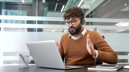 Confident businessman in a headset talking on a video call using laptop computer sitting in office. A male manager has a remote business meeting. male professional communicates at an online conference - Powered by Adobe