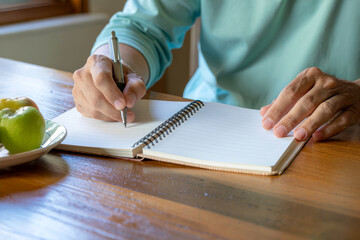 Hands writing in a notebook on a wooden table