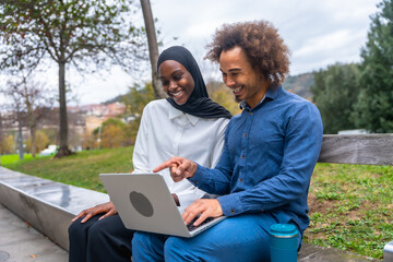 Diverse couple collaborating on laptop in park