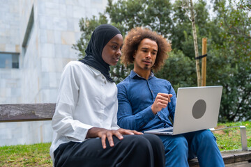Diverse couple discussing business project using laptop outdoors