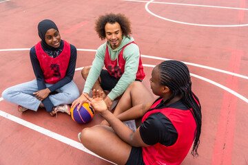 Diverse young friends relaxing and talking on basketball court