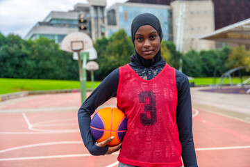 Confident young muslim woman playing basketball on court