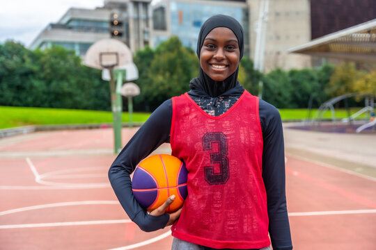 Muslim woman basketball player smiling holding ball on court