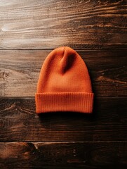 Close-up of an orange beanie lying on a wooden surface. the beanie is made of a ribbed knit fabric and has a snug fit. the color of the beanie appears to be a warm, earthy orange.