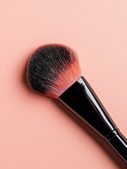 Close-up of a makeup brush on a pink background. the brush has a black handle and a round, black bristled head with red and white bristles.