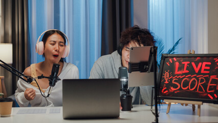 Young happy Asian couple wear headphone sit on desk online live streaming football live score...
