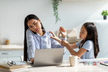 A teen girl looks upset while sitting next to her mother who is busy working from home. The mother is on a phone call and focused on her laptop, unaware of her daughter's need for attention.