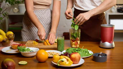 Couple preparing smoothie ingredients with fruit greens and blender jar on table. Concept of recipe creation, wellness education, smoothie tutorials, cooking course materials.