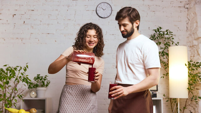 Couple pouring berry smoothie into glasses while preparing healthy drinks together. Concept of recipe tutorials, smoothie marketing assets, wellness workshops, nutrition visuals.